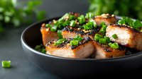 Grilled salmon fillets with black sesame crust and fresh chopped green onions served in dark ceramic bowl, close up view on modern food presentation.