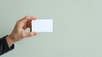 Male hand holding blank white business card against neutral gray background, suitable for branding, corporate identity, and marketing mockup designs.