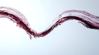 Dynamic red wine splash creating elegant wave motion against clean white background for beverage advertising and culinary design projects.