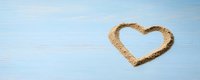 Heart shape drawn in sand on beach with blue sky and clouds background for romantic vacation and love concept.