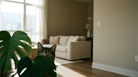 Adorable tabby cat peeking from behind green monstera plant in modern living room with natural sunlight streaming through large windows creating cozy atmosphere.