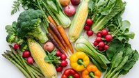 Fresh organic vegetables including broccoli, corn, carrots, radishes, bell peppers and leafy greens arranged on white background for healthy eating.