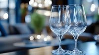 Two empty wine glasses on wooden table with blurred restaurant interior and bokeh lights in background, suitable for dining, hospitality and beverage concepts.