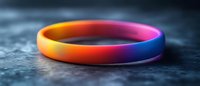Rainbow colored silicone bracelet on dark textured background with selective focus and dramatic lighting, symbolizing pride, unity and social awareness.