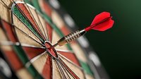 Red dart hitting bullseye on dartboard, close-up macro shot showing precision and accuracy. Strategic business concept with selective focus and blurred background.