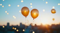 Golden balloons floating against sunset city skyline with bokeh lights creating festive atmosphere for celebration events.