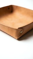 Tan leather valet tray with brass snap fasteners and visible stitching on white background, a stylish desk organizer for keys and accessories.