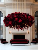 Luxurious suspended floral chandelier with red poinsettias and string lights creates dramatic focal point above burgundy velvet seating in elegant white interior space.