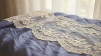 Delicate ivory lace trim draped over soft blue fabric, showcasing intricate embroidered details and ornamental edging for wedding, fashion, and textile design projects.