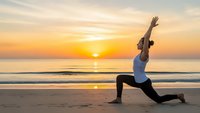 Woman practicing yoga warrior pose on beach at golden sunrise with ocean waves and peaceful sky for wellness meditation and fitness lifestyle.