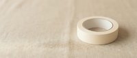 White masking tape roll on beige linen fabric background for crafting and home improvement projects.