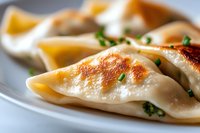 Pan-fried dumplings with golden-brown crust and fresh chives garnish on white plate, close-up macro shot showing texture and filling details in natural light.