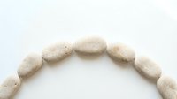 Smooth beige stone pebbles arranged in arc formation on white background, isolated spa and wellness design element for relaxation and meditation concepts.