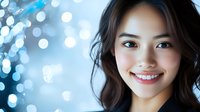 Young Asian woman with bright genuine smile against blue bokeh background, radiating happiness and confidence. Professional portrait with soft lighting.