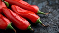 Fresh red chili peppers with water drops on dark stone background, macro shot showing vibrant color and texture, food photography for spicy cuisine.
