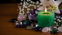 Spa wellness scene with burning green candle, healing crystals, white lily flower and baby breath on wooden surface for relaxation and meditation therapy.