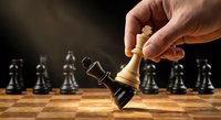Hand moving white king chess piece on wooden board with black pieces in background representing strategic business leadership and decision making.