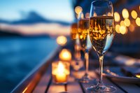 Champagne glasses with golden bubbles against blurred sunset and candlelight background create romantic atmosphere at waterfront dining setting.