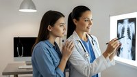 Two female healthcare professionals examining chest X-ray in modern medical office. Doctor and nurse analyzing lung radiograph for patient diagnosis.