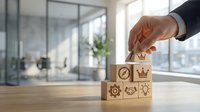 Businessman hand placing wooden block with crown icon on stack of cubes featuring business symbols in modern office with city view, representing leadership, strategy, and corporate hierarchy.