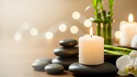 Spa wellness scene with burning candles, hot stones, bamboo and orchid flowers creating peaceful relaxation atmosphere for massage therapy treatments.
