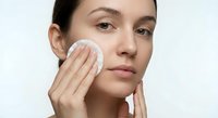 Young woman applying skincare product with cotton pad on face during daily beauty routine for healthy glowing skin and facial care regimen.