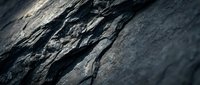 Dark gray rock surface with natural cracks and weathered texture showing geological layers and stone formation patterns for backgrounds and textures.