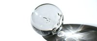 Crystal clear glass sphere with internal bubbles casting dramatic shadows and light reflections on white surface for modern decor and meditation concepts.