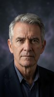 Senior man with gray hair and facial wrinkles wearing dark blazer over blue shirt, serious expression, professional headshot for corporate, business, or editorial use.