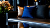 Elegant leather bench with decorative pillows in royal blue, black and tan colors creating luxurious seating arrangement in dimly lit contemporary interior space.