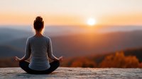 Woman practicing yoga meditation at sunrise on mountain top with peaceful valley landscape and golden hour lighting for wellness and mindfulness concepts.