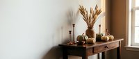 Autumn home decor with pumpkins, wheat stalks and candles on wooden console table by window creating cozy seasonal interior design atmosphere.