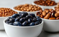 Black beans in white ceramic bowl with assorted nuts and legumes in background, selective focus on foreground, macro food photography for healthy eating blogs.