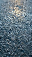 Close-up of sandy beach surface with golden sunlight reflecting off wet sand and small pebbles, suitable for travel and nature backgrounds.