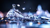 Macro photography of water splash with bokeh lights creating dynamic motion effect. Crystal clear liquid crown formation against dark background with blue reflections.