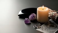 Mystical altar setup with burning candle, amethyst crystals, pentagram symbol, tarot cards and ritual bowl for spiritual practices and meditation.