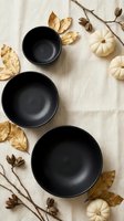 Black ceramic bowls arranged with autumn leaves, white pumpkins and dried branches on linen fabric for seasonal table setting and fall home decor styling.
