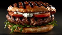 Juicy grilled beef burger with fresh tomato slices, arugula leaves and creamy sauce on toasted brioche bun against dark background. Close up food photography.
