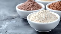 Different types of protein powder supplements in white ceramic bowls on dark concrete background, sports nutrition and healthy lifestyle concept.