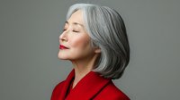 Elegant mature Asian woman with silver gray hair and red coat in profile view against neutral background, eyes closed with serene peaceful expression.