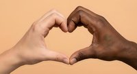 Two diverse hands forming heart shape symbol representing unity, love and racial harmony against warm beige background for social campaigns.