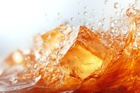 Ice cube splashing in amber liquid with dynamic water drops and waves creating refreshing movement against light background. Perfect for beverage advertising.
