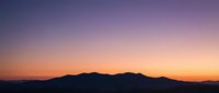 Dramatic sunset sky with vibrant purple and orange gradient colors over dark mountain silhouettes creating peaceful twilight landscape scenery.