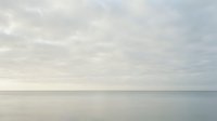 Serene seascape with calm waters and overcast sky, minimalist coastal landscape with soft gray tones, tranquil ocean horizon for meditation and wellness design.