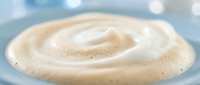 Creamy white cosmetic cream swirl with smooth texture against soft blue background for skincare and beauty product applications.