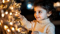 Young girl in cozy sweater decorating Christmas tree with warm golden lights creating magical holiday atmosphere for family celebrations.