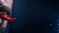 Surreal portrait of bearded man with red hot chili pepper replacing lips against dark background with glowing particles and copy space.