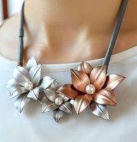Elegant floral necklace with metallic silver and rose gold leather flowers adorned with pearl centers on gray cord, showcasing delicate handcrafted artistry.