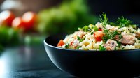 Fresh quinoa salad with diced vegetables, herbs and protein in black bowl on kitchen counter for healthy meal preparation and nutritious dining.