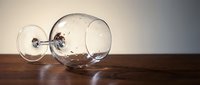 Broken wine glass lying on wooden table with scattered fragments, symbolizing fragility and accidents in dining or celebration contexts.